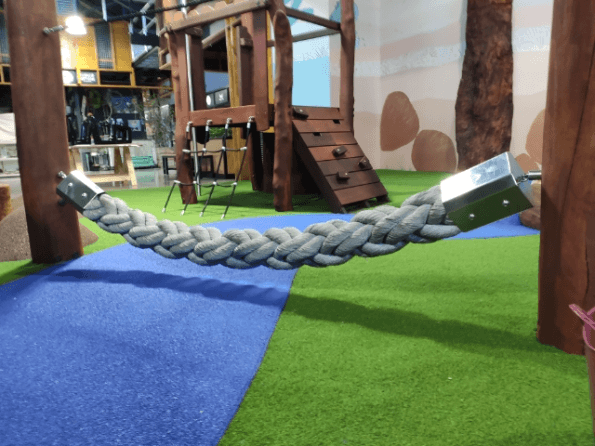 White plaited rope linking between two timber pillars with timber play fort in background